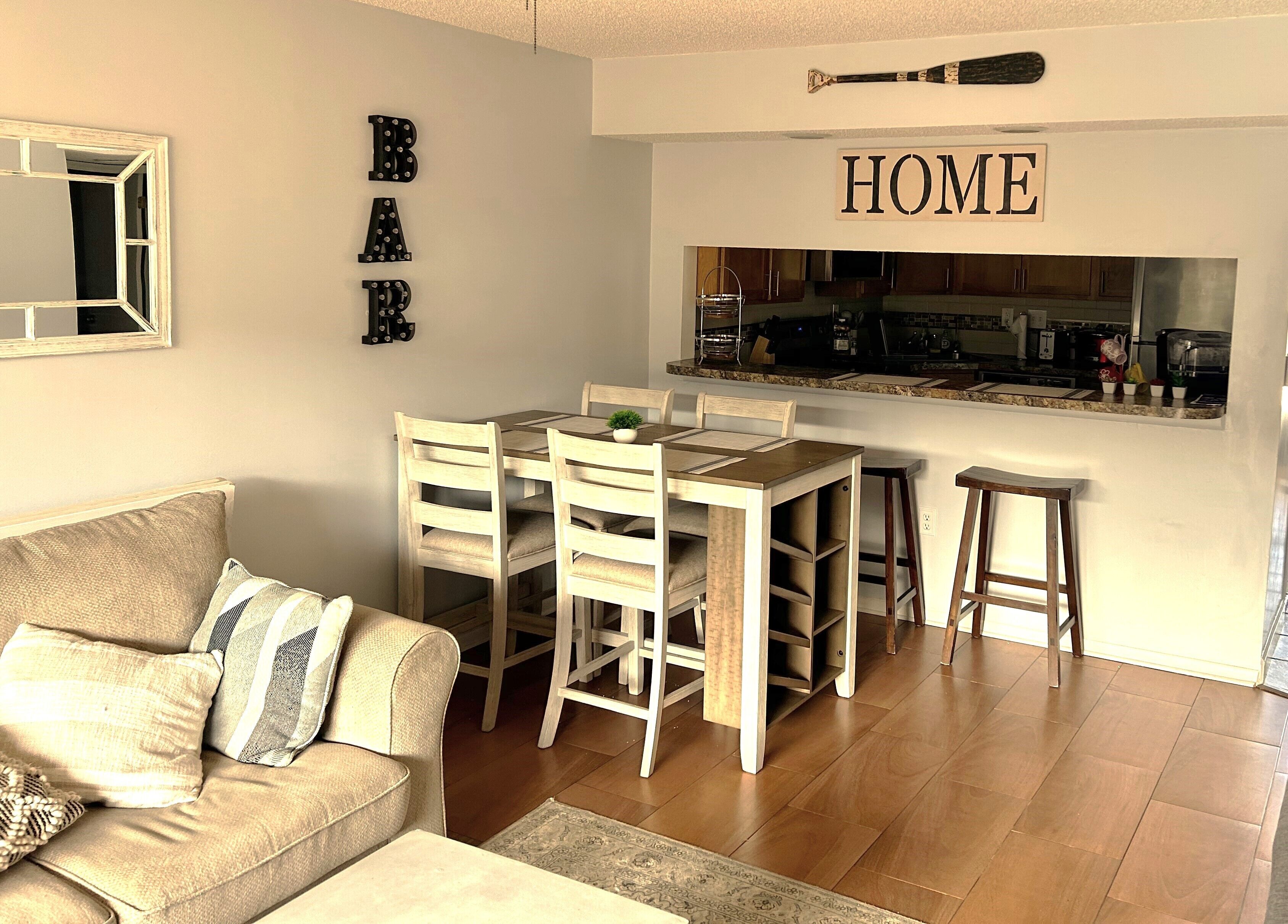 Un soggiorno con divano, un tavolo da pranzo con sedie, angolo cottura e un cartello con la scritta 'HOME'.