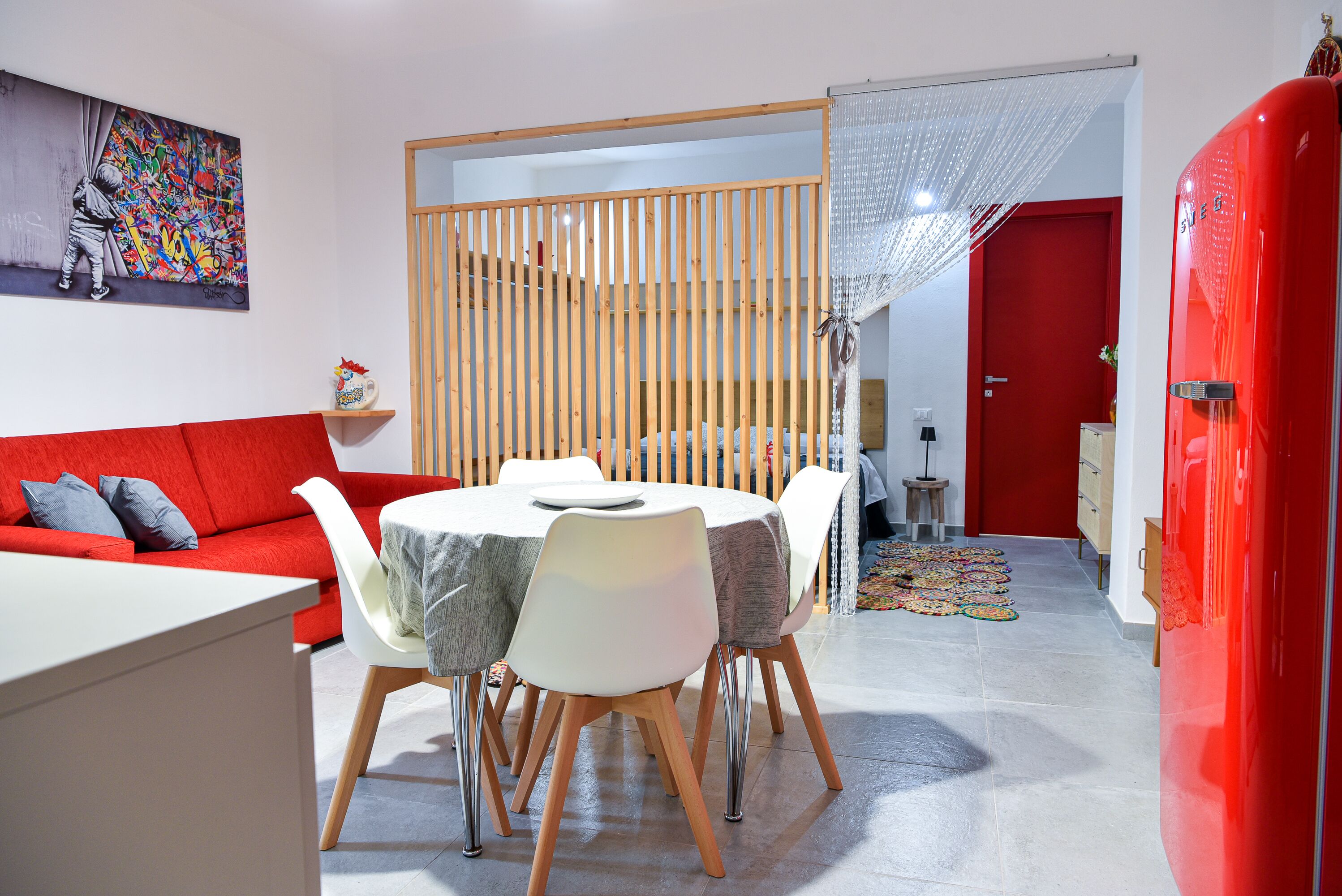 A modern living space with a red sofa, white dining table, and a colorful rug.