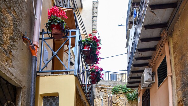 Una escalera estrecha de piedra que sube hacia un edificio con fachada amarilla y una pequeña ventana.