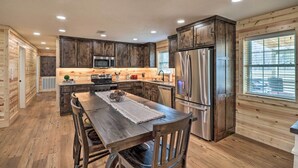 A modern kitchen with wooden cabinetry, stainless steel appliances, and a dining area with a wooden table and chairs. - Greers Ferry Home on 40 Acres 1/4 Mi to Lake! (Greers Ferry)