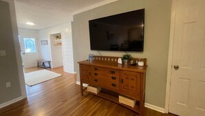 A spacious living room with hardwood floors, a wooden entertainment center, and a large flat-screen TV mounted on the wall. - POOL house with FENCED Yard for Pets, by the ARK Encounter, Airport, Cincinnati (Independence)