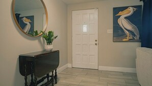 Un couloir avec une porte blanche, un miroir rond, une console en bois foncé et une plante en pot.