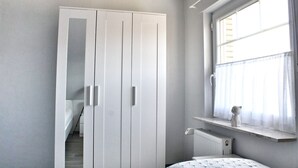 Quarto com armário branco, janela com cortinas e radiador.
