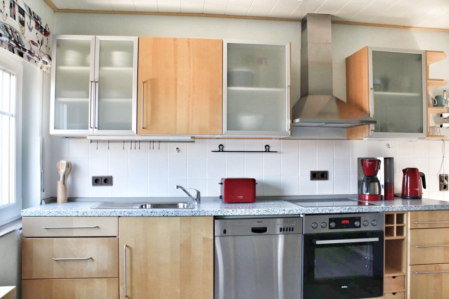 A modern kitchen with wooden cabinets, a stainless steel dishwasher, and a red coffee maker.