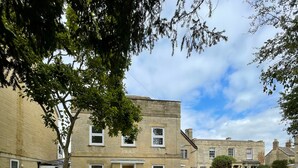 A courtyard with a cobblestone path, a grassy area, and a two-story building with multiple windows and a door. - Lovely Two Bedroom Home (Kidlington)