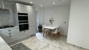 A modern kitchen with white cabinets, a built-in oven, and a dining area with a white table and chairs. - Lovely Two Bedroom Home (Kidlington)