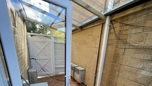 A covered patio with a wooden deck, a white door, and a garage door. - Lovely Two Bedroom Home (Kidlington)