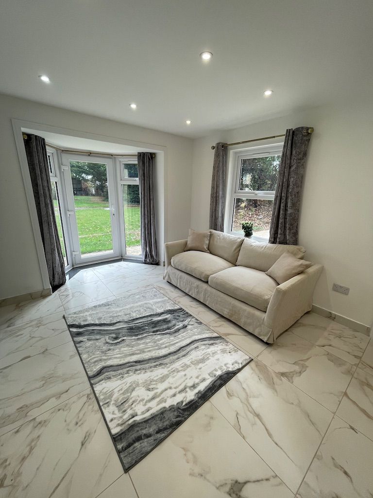 A room with a beige sofa, a patterned rug, and a large window with curtains.