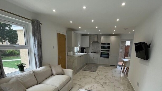 A modern living room with a sofa, a patterned rug, and a kitchen in the background. - Lovely Two Bedroom Home (Kidlington)