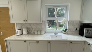 A modern kitchen with grey cabinets, a marble countertop, a window, and a sink. - Lovely Two Bedroom Home (Kidlington)
