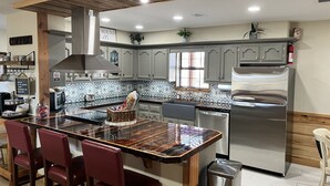 A modern kitchen with a central island, stainless steel appliances, and a wooden ceiling.