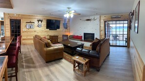 A cozy living room with a wooden interior, a fireplace, a television, and a dining area with a glass table and leather chairs.