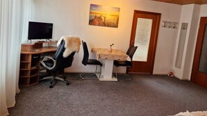 Une pièce avec un plafond en bois, un bureau avec un ordinateur, deux chaises, une petite table avec un vase et un tableau accroché au mur.