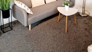 Un salon moderne avec un canapé gris, une petite table blanche, un lampadaire et un grand tableau représentant une scène de plage.