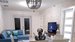 A dining area with a table set for two, a blue sofa, and a television in the background. - Viamarhe-3/1 Ground Level Oceanfront home w/Kayaks, Yard Games & More (Marathon)