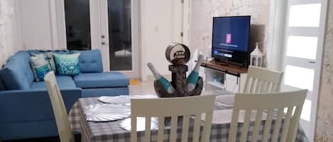 A dining area with a table set for two, a blue sofa, and a television in the background.