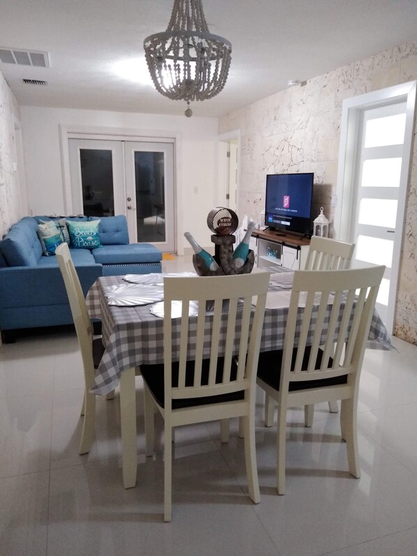 A dining area with a table set for two, a blue sofa, and a television in the background.