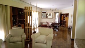 Ein geräumiges Wohnzimmer mit einer hölzernen Spielanlage, zwei weißen Sesseln, einem Essbereich mit Tisch und Stühlen sowie einem Bücherregal.