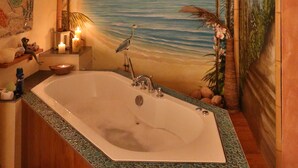 Ein Badezimmer mit einer großen Badewanne, einer Wandmalerei mit einer Strandansicht und einem kleinen Tisch mit Kerzen.