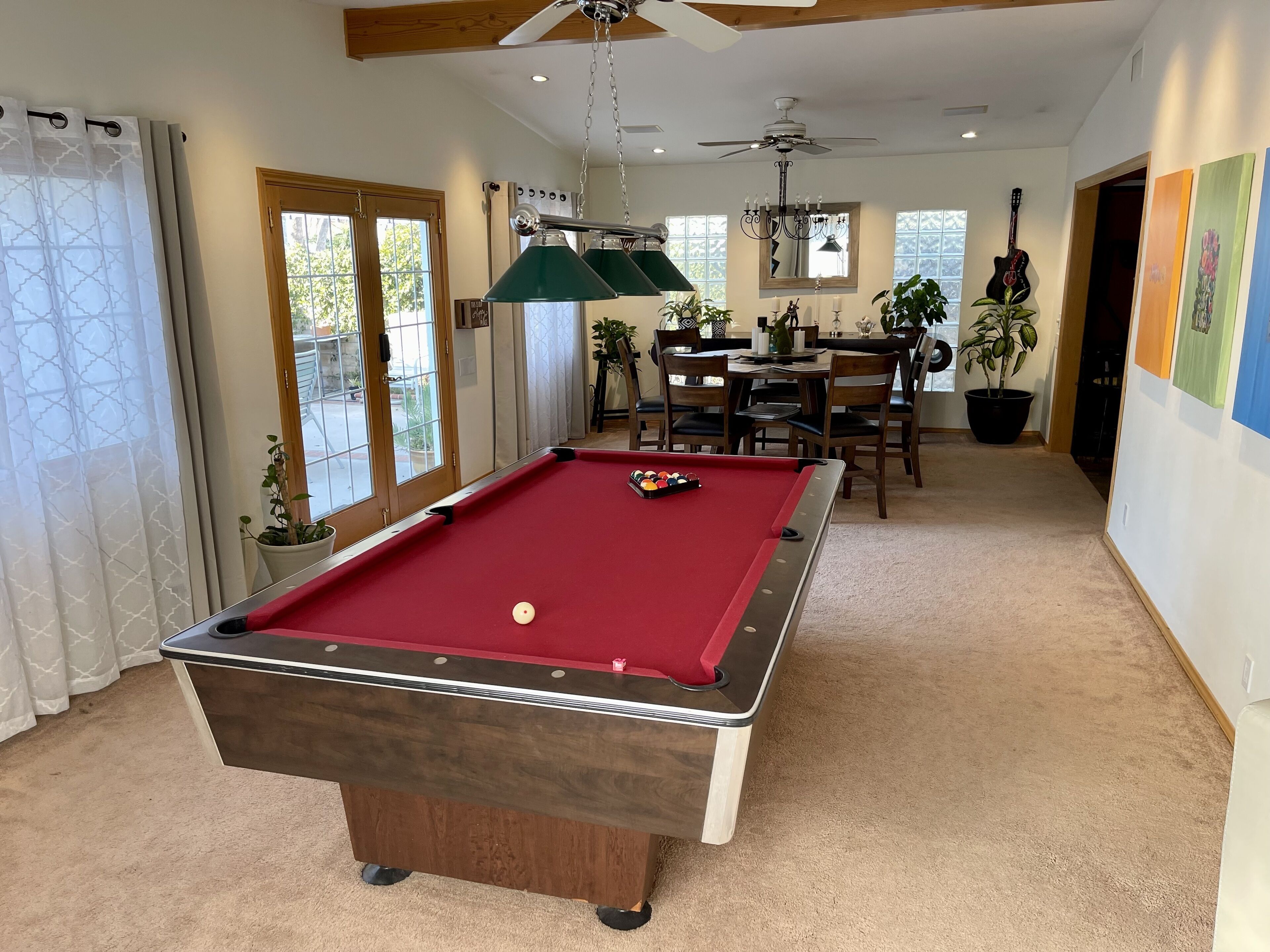 A pool table in a room with a ceiling fan, a dining area, and a view of the outdoors.