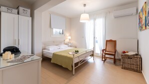 A bedroom with a bed, bedside table, lamp, chair, wicker basket, and a window with curtains. - Aurora Villa II with private Jacuzzi - Naxos (Agios Prokopios)
