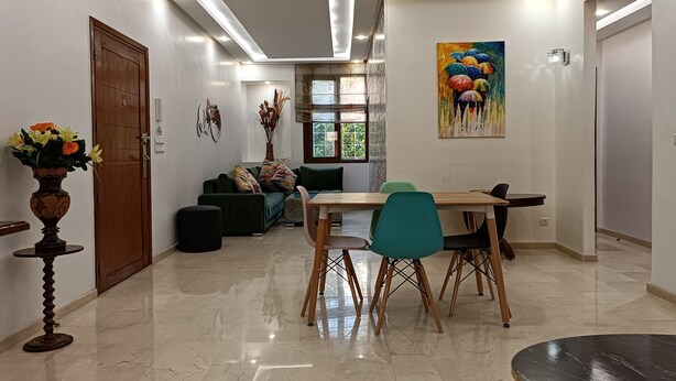 A modern living room with a dining area, a wooden door, a vase with flowers, and a painting on the wall. - Luxury Family House with Garden View Casablanca (Dar-el-Beida)