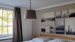 A bedroom with a wooden bed, striped bedding, a hanging lamp, and a window with curtains.