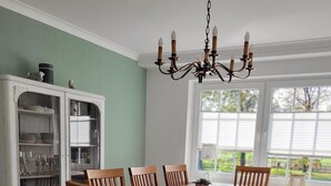 A dining room with a wooden table and chairs, a white cabinet with glass doors, and a chandelier.