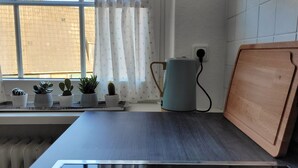 A kitchen with a window, a kettle, and a cutting board.