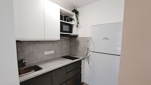 A compact kitchen with white cabinets, a stainless steel sink, a microwave, and a refrigerator. - Casa Helena (Costa Calma)