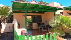 A covered outdoor seating area with a table and chairs, a small trash bin, and a sign indicating a room number. - Casa Helena (Costa Calma)
