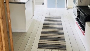 A kitchen with white cabinets, a stove, and a microwave. There is a striped rug on the floor. - In the footsteps of Astrid Lindgren - vacation home with 110 sqm (Trånshult)