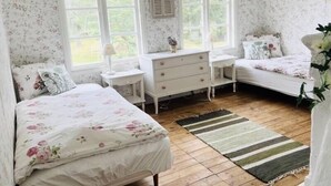 A bedroom with floral wallpaper, two beds, a dresser, and a window with shutters. - In the footsteps of Astrid Lindgren - vacation home with 110 sqm (Trånshult)