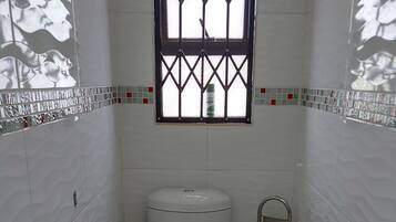Un baño pequeño y moderno con inodoro, bidé y ventana con reja metálica.