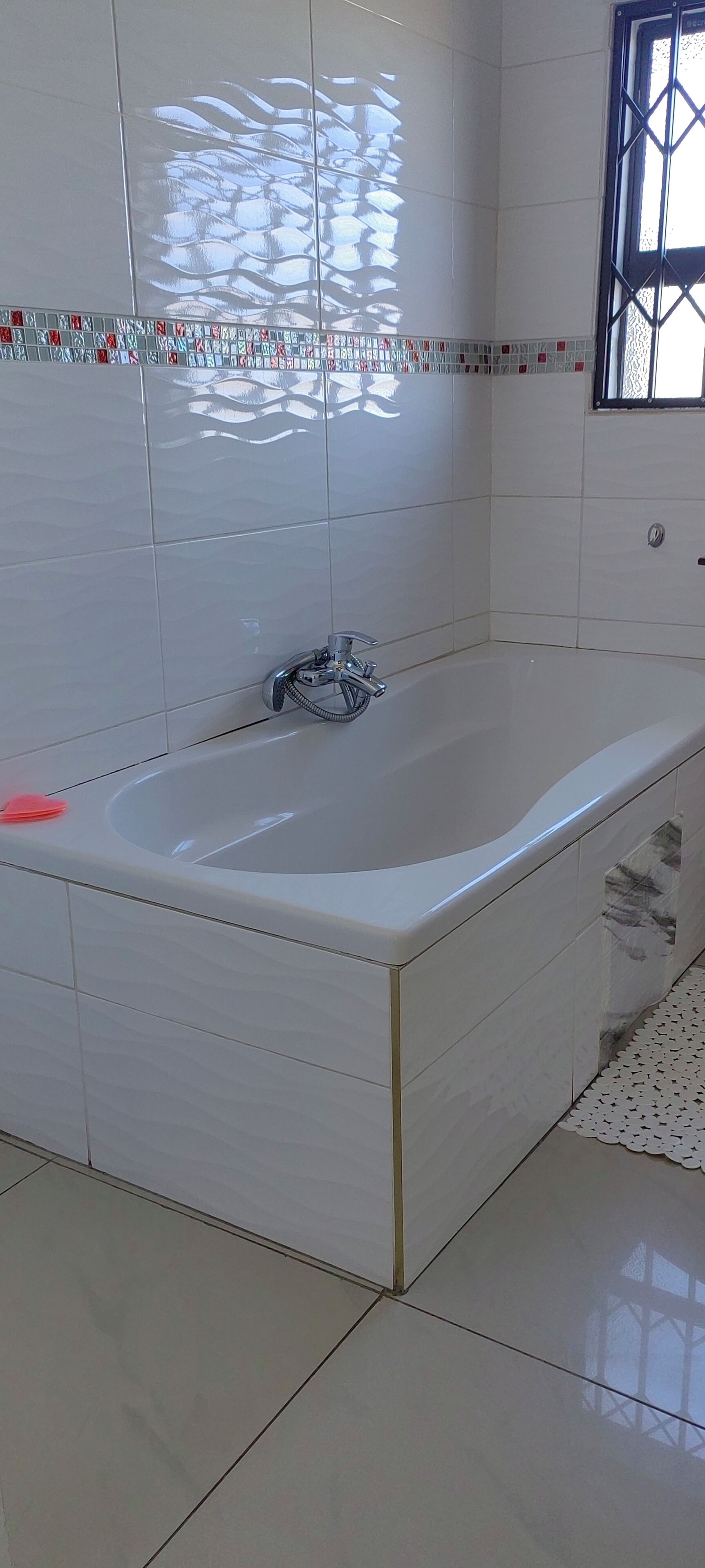 A bathroom with a bathtub, white tiled walls, and a window with a metal grille.