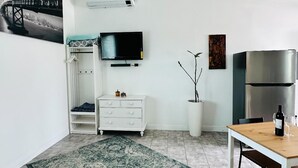 A compact living space with a kitchenette, a flat-screen TV mounted on the wall, a white dresser, a dining table with a bottle of wine, and a potted plant. - Beautiful place and view to rest and clear your mind.#1 (Antioch)