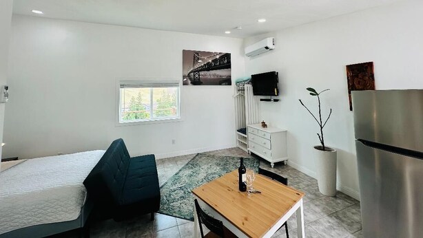 A modern, well-lit room with a bed, a wooden table with a bottle and glass, a TV, a refrigerator, and a window with a view of a bridge. - Beautiful place and view to rest and clear your mind.#1 (Antioch)