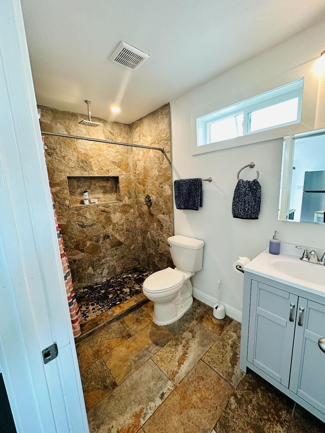 A bathroom with a stone shower, a toilet, a sink, and a mirror.