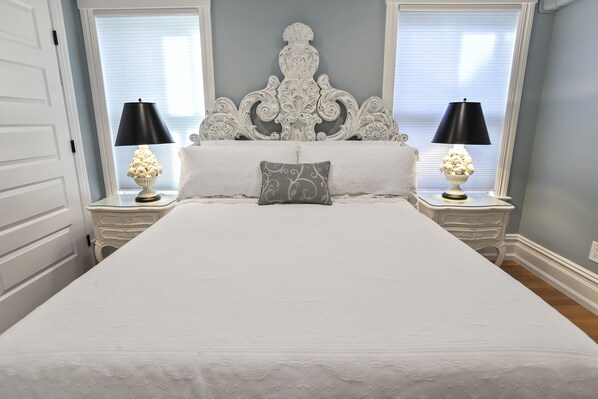 A neatly made bed with a decorative headboard, two bedside tables with lamps, and a window with blinds.