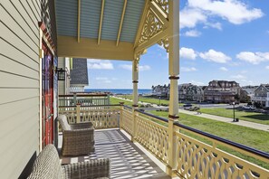 A balcony with wicker furniture, a view of the beach, and residential buildings in the background.