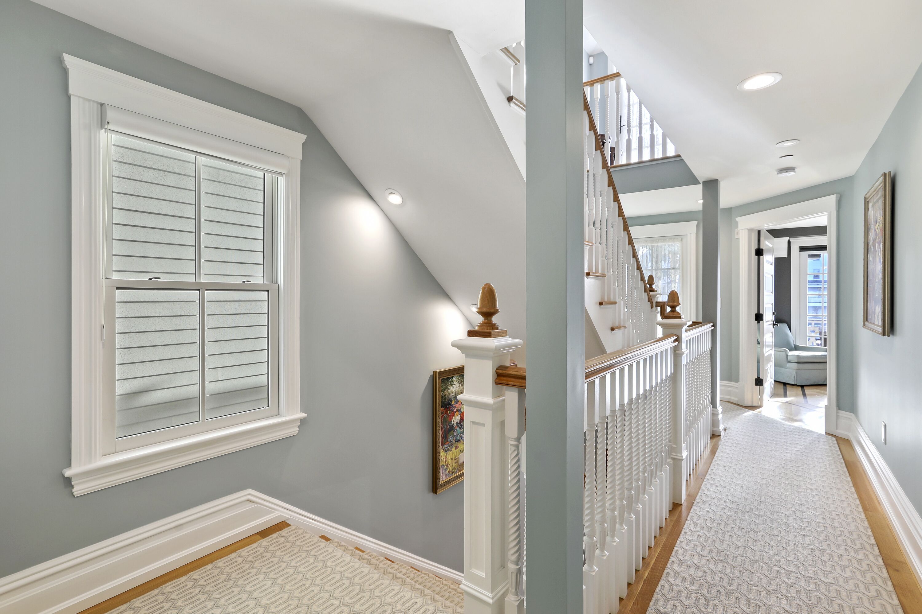 A hallway with a wooden staircase, white railings, and a patterned rug.