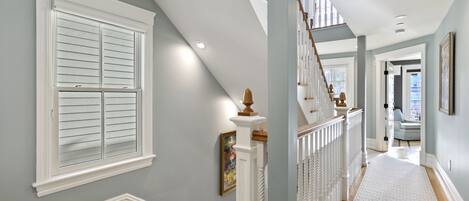 A hallway with a wooden staircase, white railings, and a patterned rug.