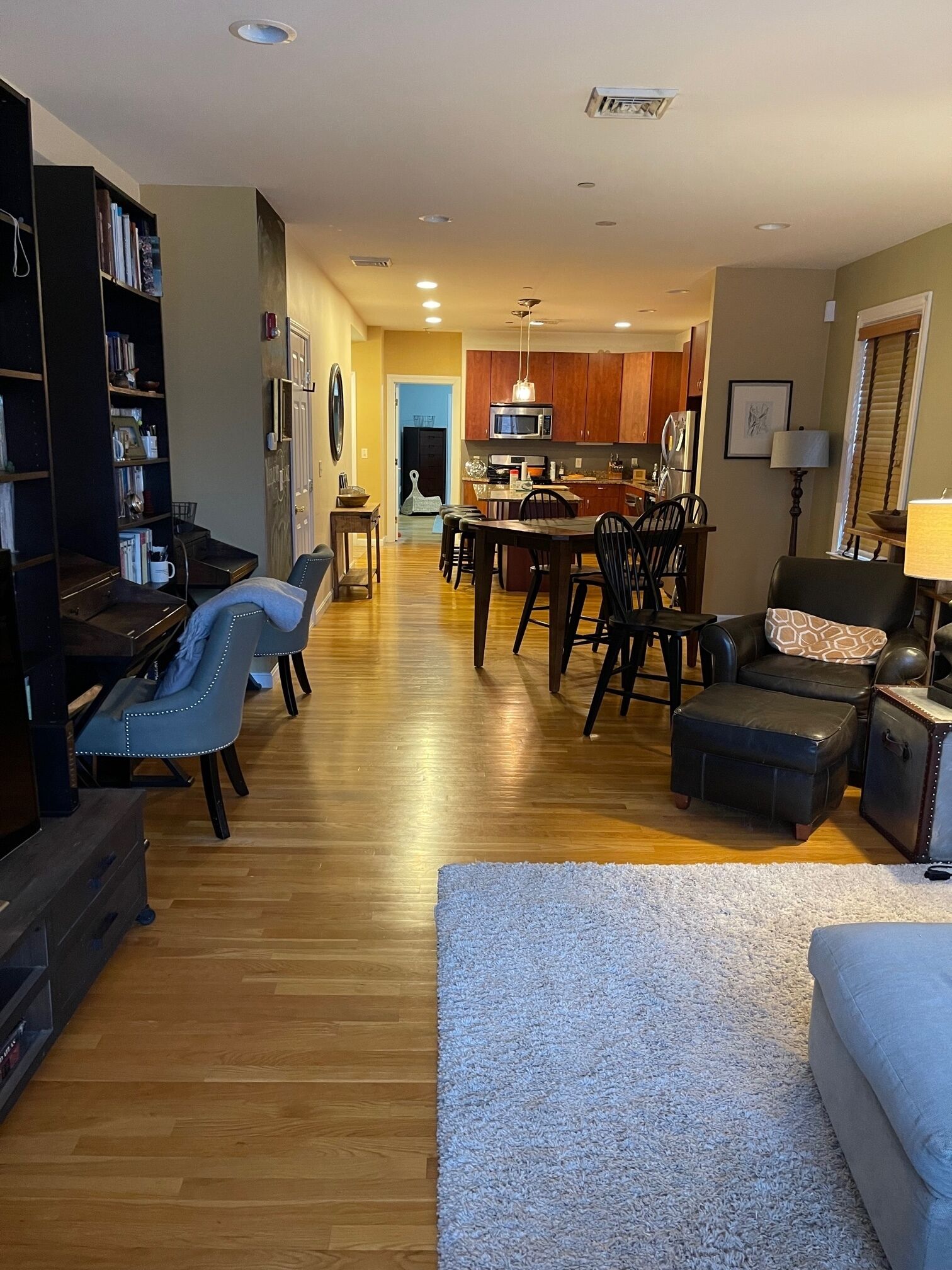 A spacious living room with a wooden floor, a dining area with a central island, and a kitchen in the background.