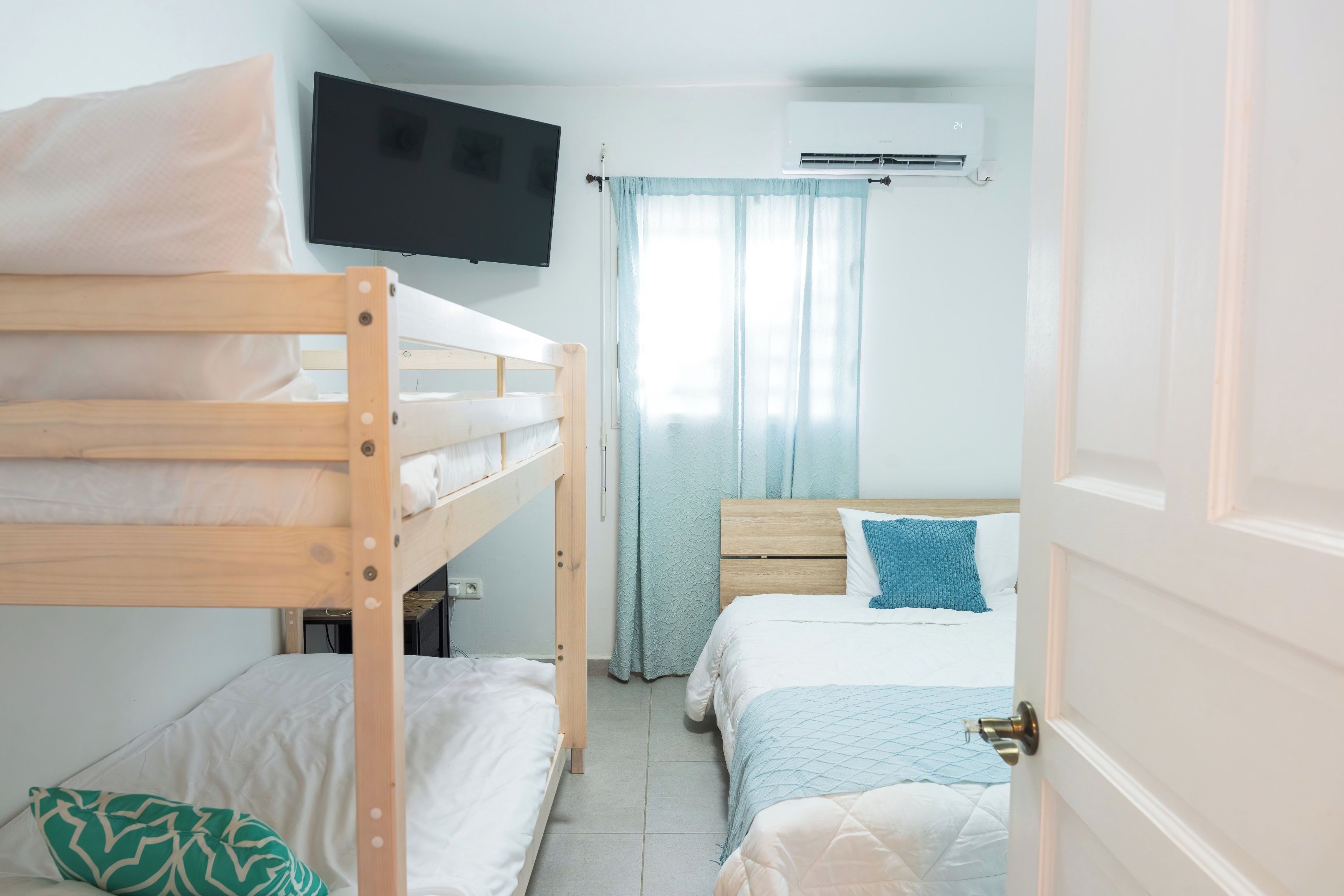 A bedroom with bunk beds, a television, an air conditioning unit, and a door.
