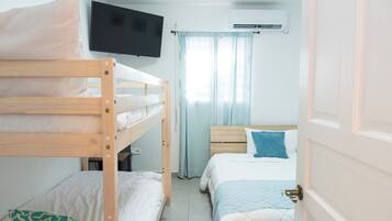 A bedroom with bunk beds, a television, an air conditioning unit, and a door.
