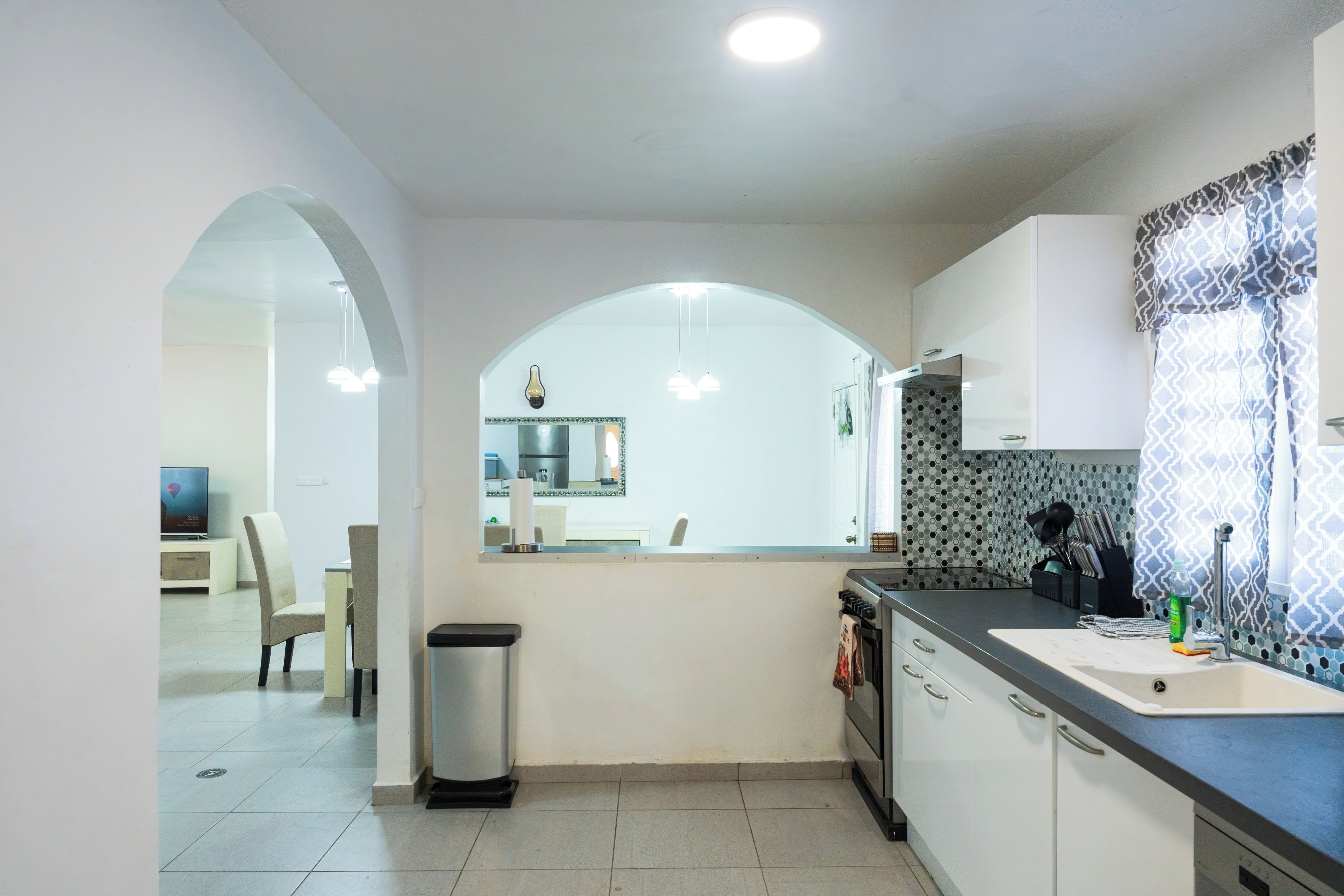 A modern kitchen with a central island, a dining area with a chair, and a trash bin.