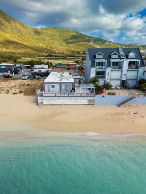 A beachfront property with a large building, a sandy beach, and a clear view of the ocean. - Novels Villa is a family-friendly home with the Caribbean Sea as your backyard. (Grand-Case)