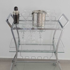 Ein klarer Glas-Barwagen mit mehreren Weingläsern und einem Metallbehälter.