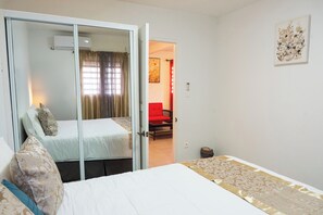 Une chambre d’hôtel avec un lit, une armoire, un fauteuil rouge et un tableau au mur.