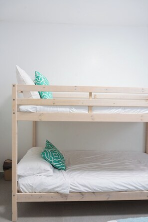 Een stapelbed met twee niveaus, elk voorzien van witte beddengoed en groene kussens met een patroon.